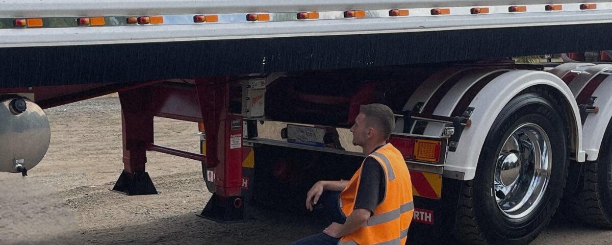 Truck driver inspecting trailer landing gear in yard during setup